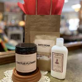 Gift set with cactus flower candle, bath soak, and hand cream beside a kraft gift bag with red tissue paper.