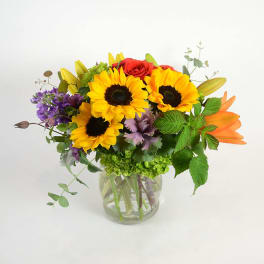 Mixed bouquet with sunflowers, roses, and lilies in a clear glass vase