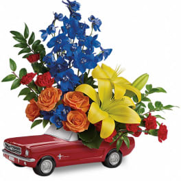 Flowers arranged in a red toy car with blue, yellow, orange, and red blooms