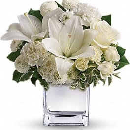 Compact white lily, rose, carnation, and mum arrangement in a clear glass cube vase