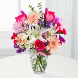 Mixed bouquet of pink, white, peach, and purple flowers in a glass vase