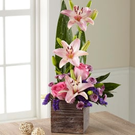 Pink lilies and roses arranged in a wooden cube vase