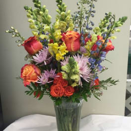 Mixed bouquet of roses, snapdragons, and purple blooms in a clear glass vase