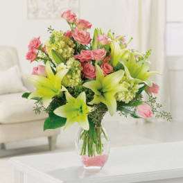 Yellow lilies and pink roses arranged in a clear glass vase with pink stones