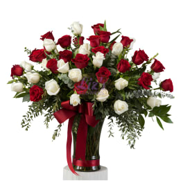 Red and white roses arranged in a tall glass vase with a red ribbon