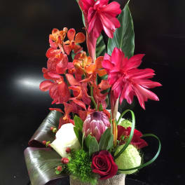 Tropical floral arrangement with pink orchids and red roses in a wrapped container