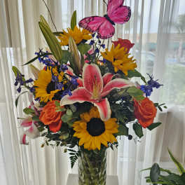Bright mixed bouquet in a glass vase with a pink butterfly pick