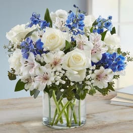 White roses and blue flowers arranged in a clear glass vase