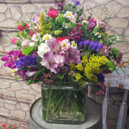 Mixed bouquet of pink, purple, white, and yellow flowers in a glass vase