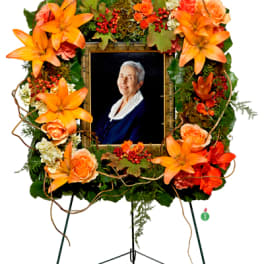 Orange floral sympathy wreath around a framed portrait on an easel