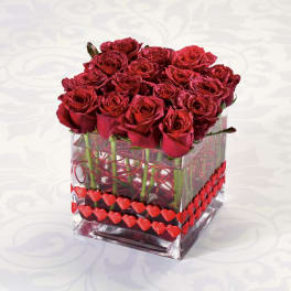 Red roses arranged in a clear square vase with heart decorations