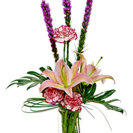 Pink lilies and carnations in a clear glass vase with tall purple spikes