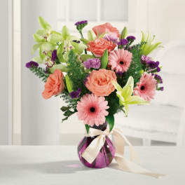 Pink and coral flowers in a purple glass vase with a ribbon
