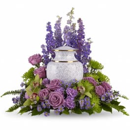 Lavender roses and purple flowers arranged around a white urn