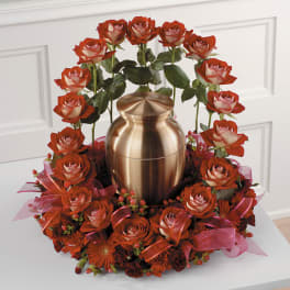 Red roses arranged around a bronze urn with pink ribbon accents