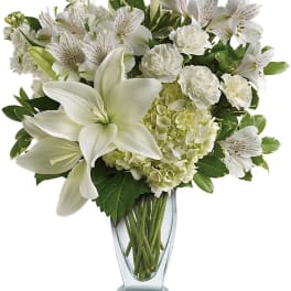 White lilies and mixed white flowers in a clear glass vase