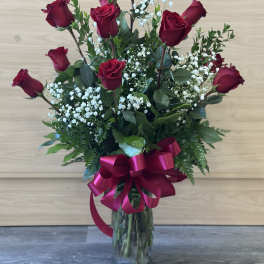 Red roses arranged in a clear glass vase with a pink ribbon bow