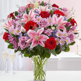 Mixed bouquet of pink lilies, red roses, and lavender flowers in a glass vase