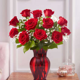 Red roses arranged in a red glass vase with white filler flowers
