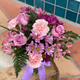 Pink and purple bouquet in a glass vase with a lavender ribbon