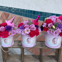 Three unicorn-themed flower buckets filled with pink and purple blooms