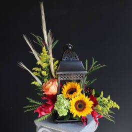 Lantern centerpiece with sunflowers, roses, and mixed foliage