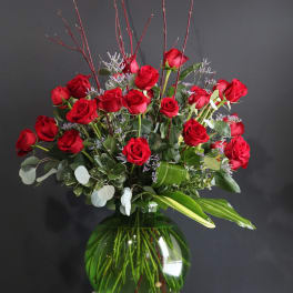 Red roses arranged in a green glass vase with purple filler and branches