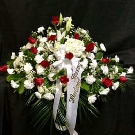 Red and white funeral spray with ribbon on a dark background