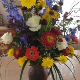 Tall mixed flower arrangement in a brown vase with blue, yellow, red, and white blooms