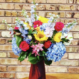 Mixed bouquet in a red vase with roses, hydrangeas, sunflowers, and lilies