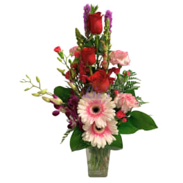 Mixed bouquet with red roses, pink gerberas, and purple orchids in a glass vase