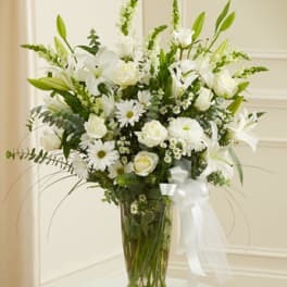 White lilies and roses in a glass vase with a white ribbon