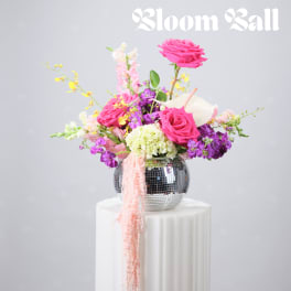 Bright pink and purple floral arrangement in a mirrored vase on a white pedestal
