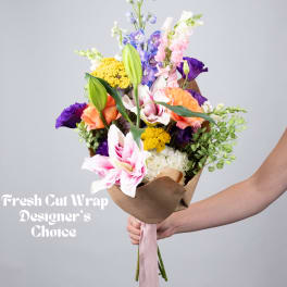 Hand-tied bouquet of mixed flowers in brown paper with a pink ribbon