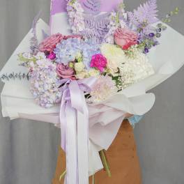 Pastel bouquet of hydrangeas, roses, and chrysanthemums wrapped in white paper