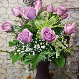 Lavender roses with baby's breath in a purple vase with a light green ribbon bow