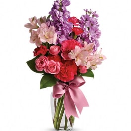 Pink and purple mixed bouquet in a clear glass vase with a satin ribbon
