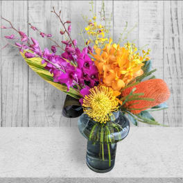 Colorful tropical bouquet in a glass vase with purple, orange, and yellow blooms