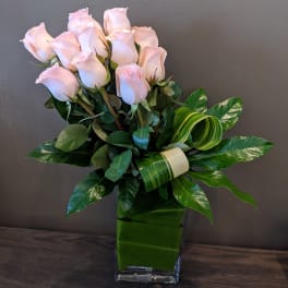 Light pink roses in a green glass vase with glossy leaves
