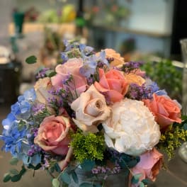 Mixed bouquet of pastel roses and blue flowers in a gray container