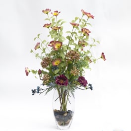 Tall floral arrangement in a clear glass vase with purple and yellow blooms