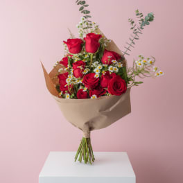 Bouquet of red roses and small white daisies wrapped in brown paper