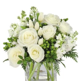 White roses and tulips with green berries arranged in a clear glass cube vase.