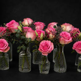 Pink roses arranged in small clear glass vases with greenery