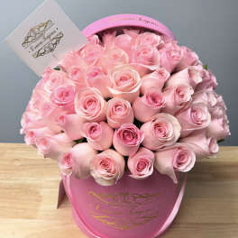 Pink roses arranged in a round pink hat box with a card attached