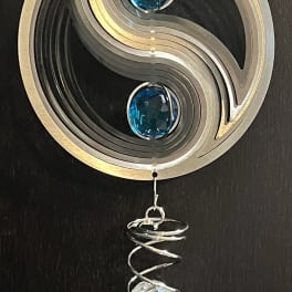 Metal wind chime with blue and clear crystal accents hanging on a dark surface