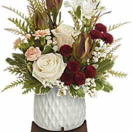 Compact arrangement of white roses, burgundy mums, and peach carnations in a white pot on a wooden stand.