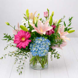 Mixed bouquet with pink lilies, blue hydrangea, and a pink gerbera daisy in a glass vase