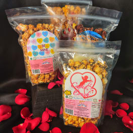 Three bags of flavored popcorn with rose petals scattered around them