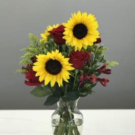 Sunflowers, red roses, and red alstroemeria in a clear glass vase